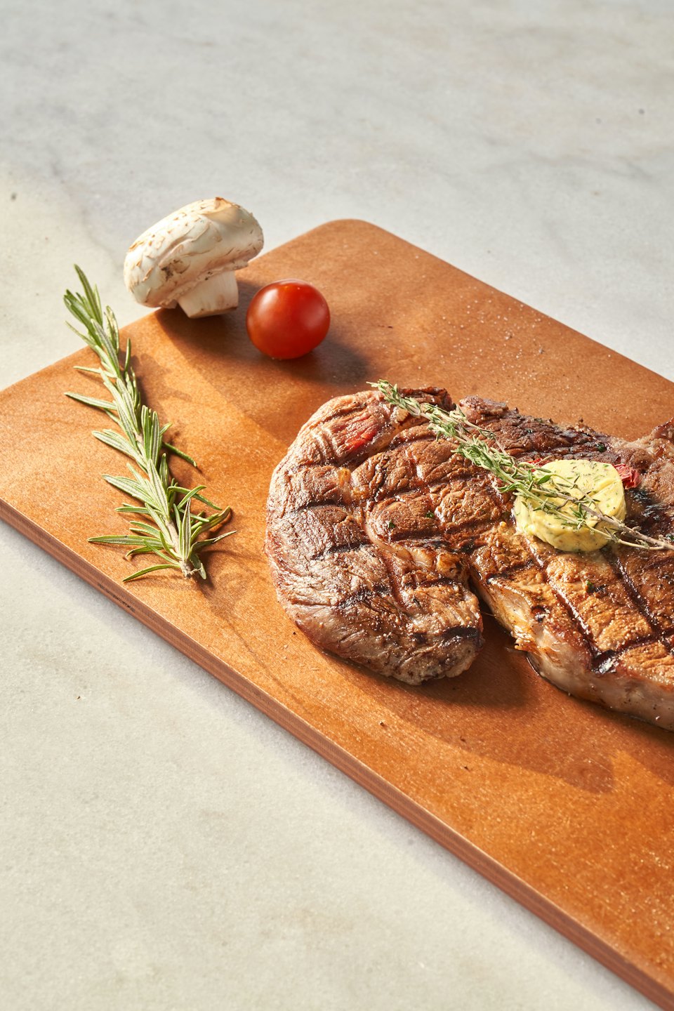 Bistecca alla griglia con burro alle erbe e timo su un tagliere di legno.