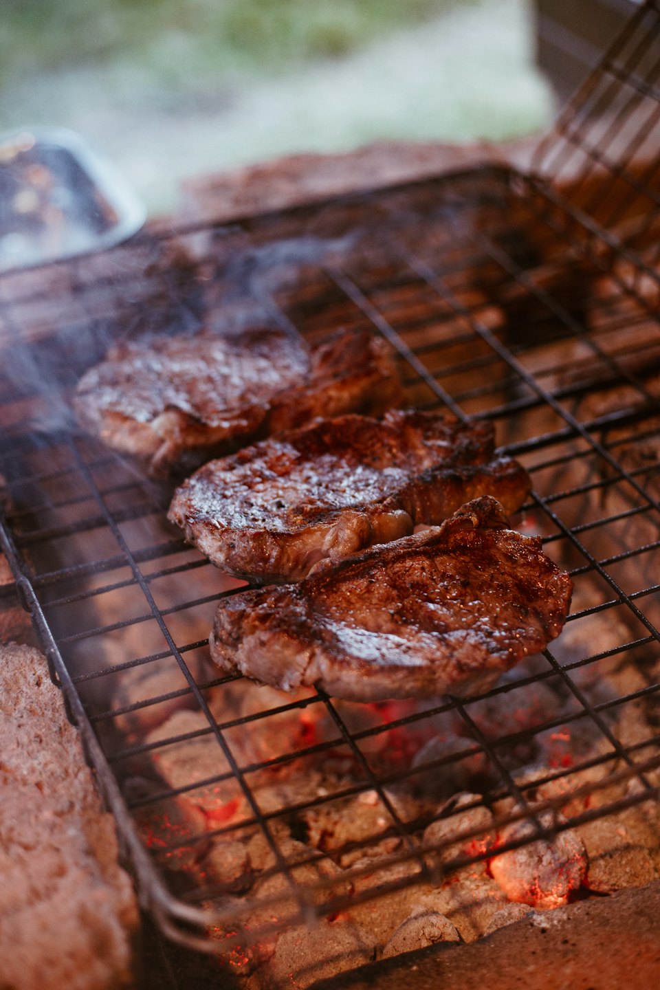 Quattro bistecche spesse grigliano su un barbecue su carboni ardenti.