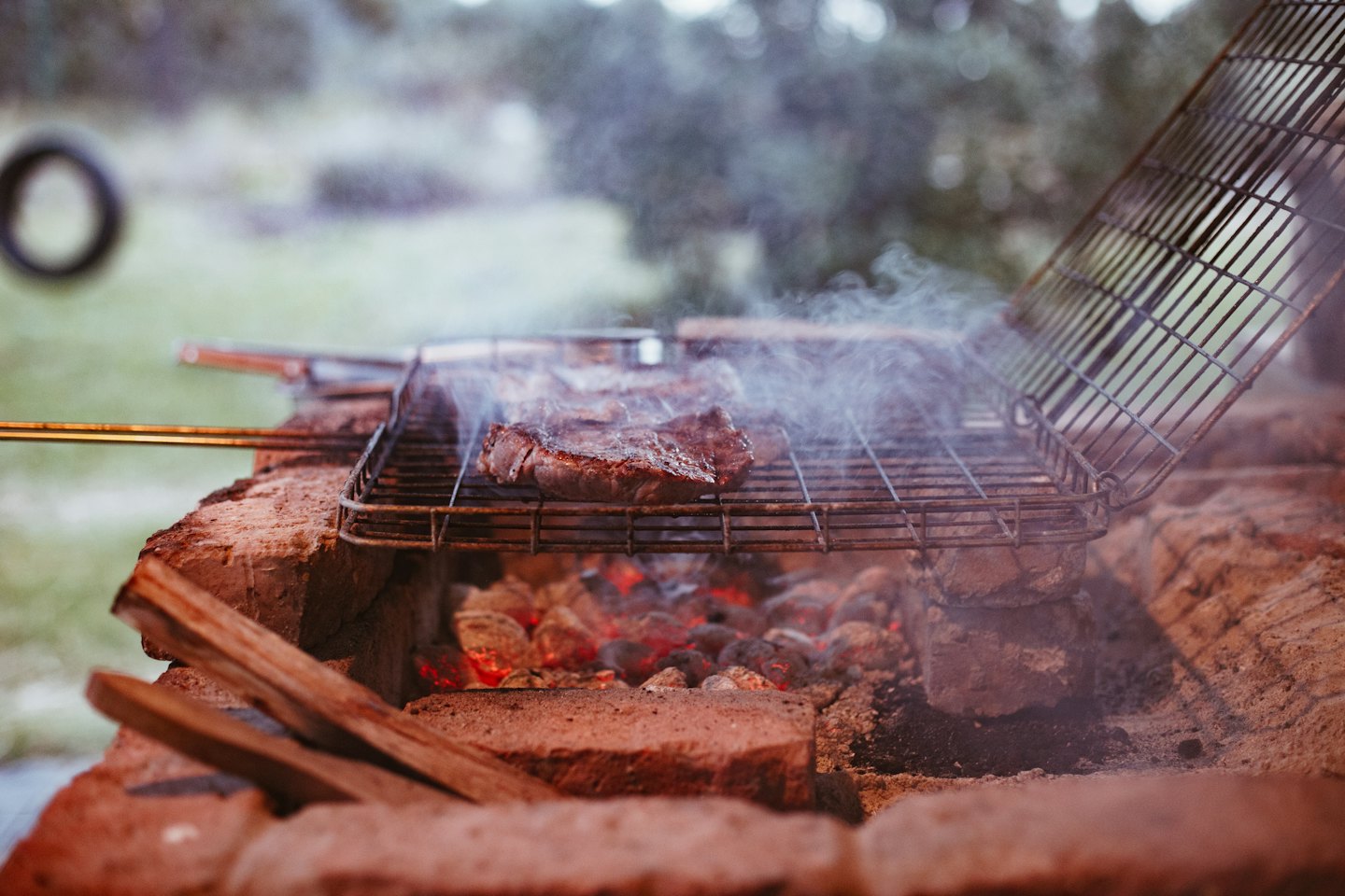 Bistecca succulenta che sfrigola su una griglia rustica di mattoni con fumo che sale.