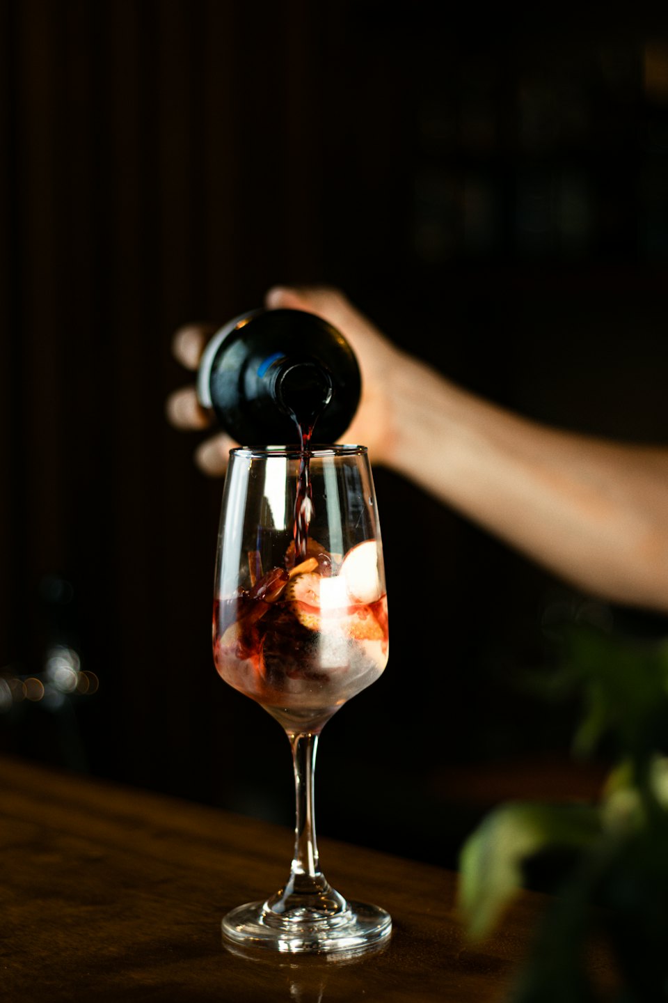 Una mano versa un cocktail rosso in un bicchiere con frutta.
