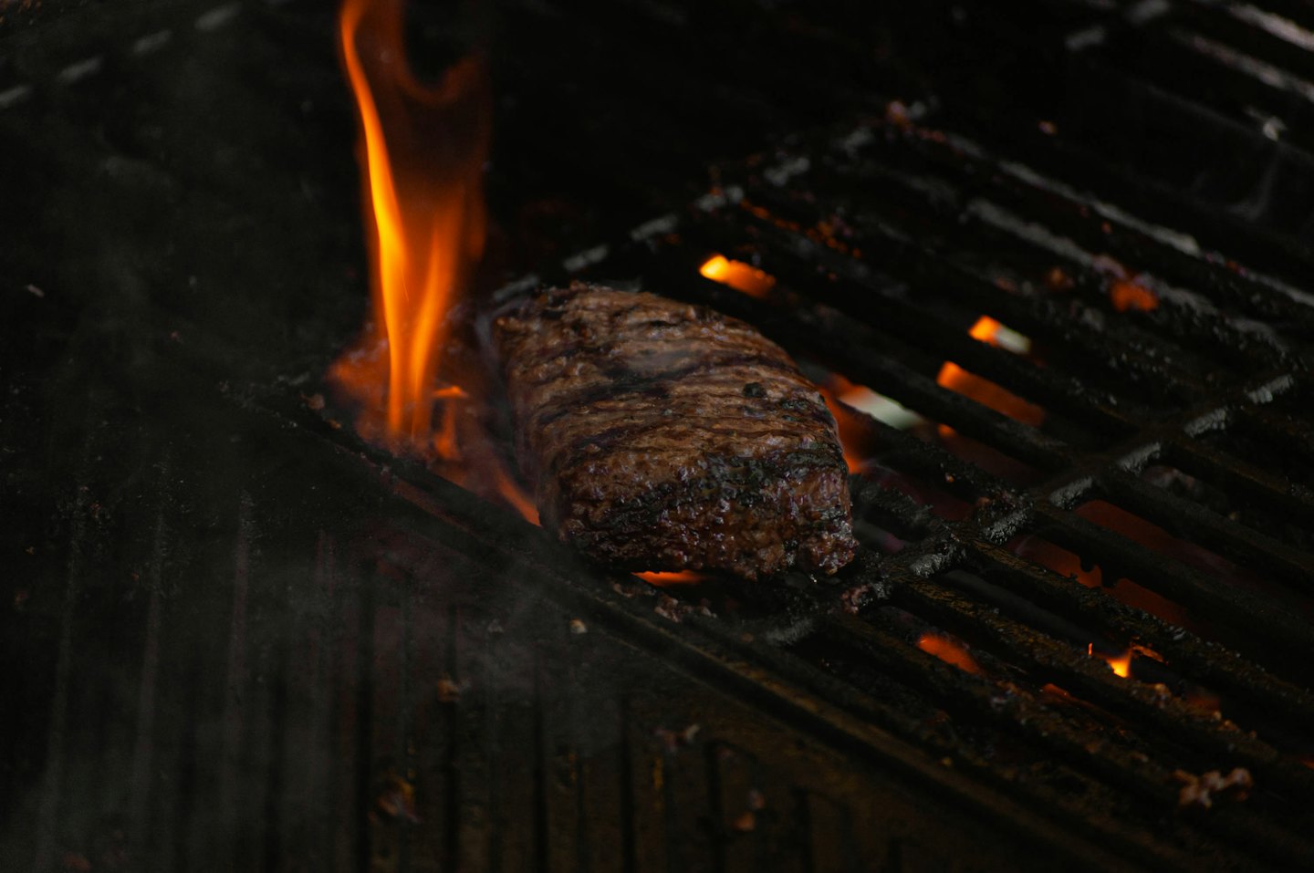 Bistecca spessa che sfrigola su una griglia calda con fiamme che si alzano.